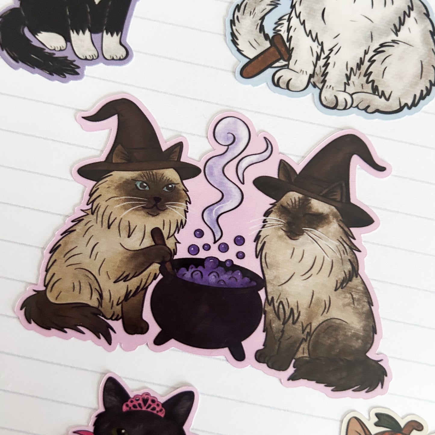 Sticker of cats in witch hats and a cauldron on lined paper