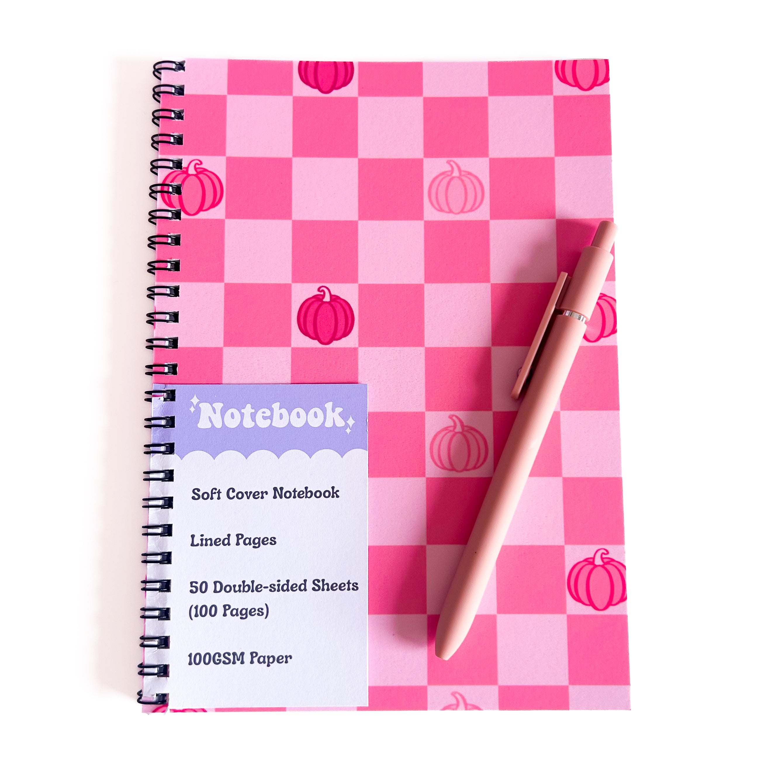 Notebook with pink checkered cover and pumpkin design, accompanied by a pen on a white background.