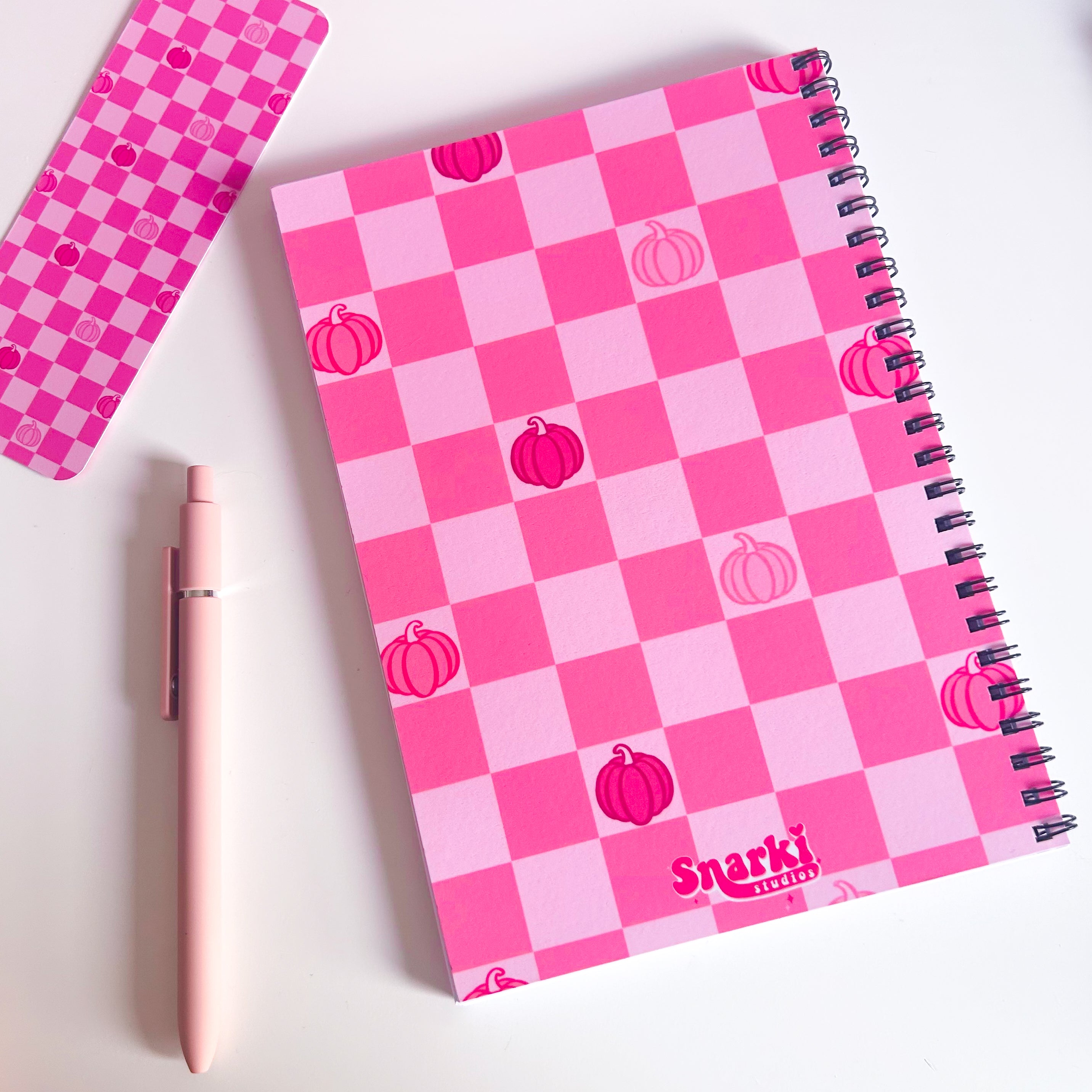 Pink checkered notebook with pumpkin designs and 'Snarki' branding on a white background
