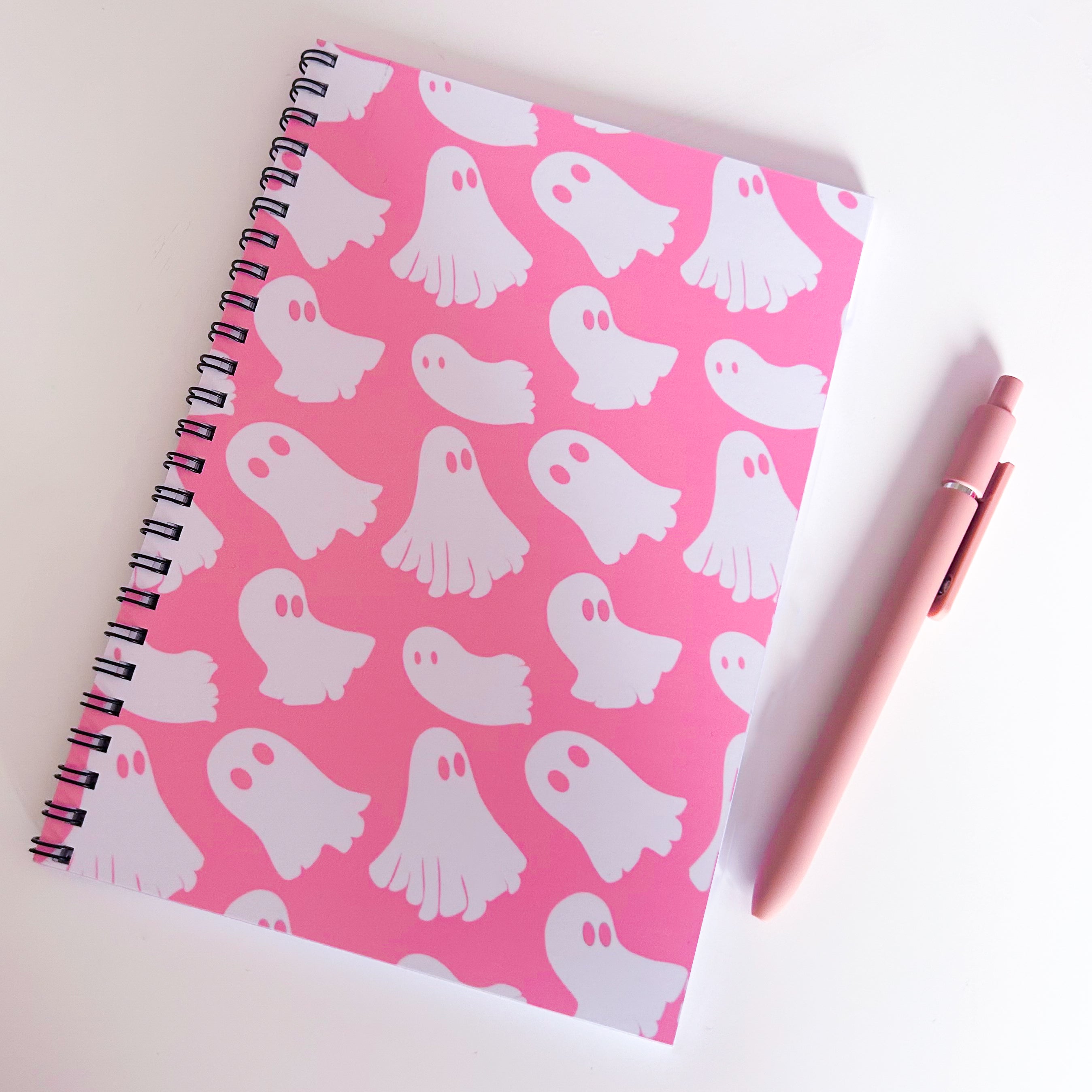 Notebook with white ghost pattern on pink cover, accompanied by a pink pen.