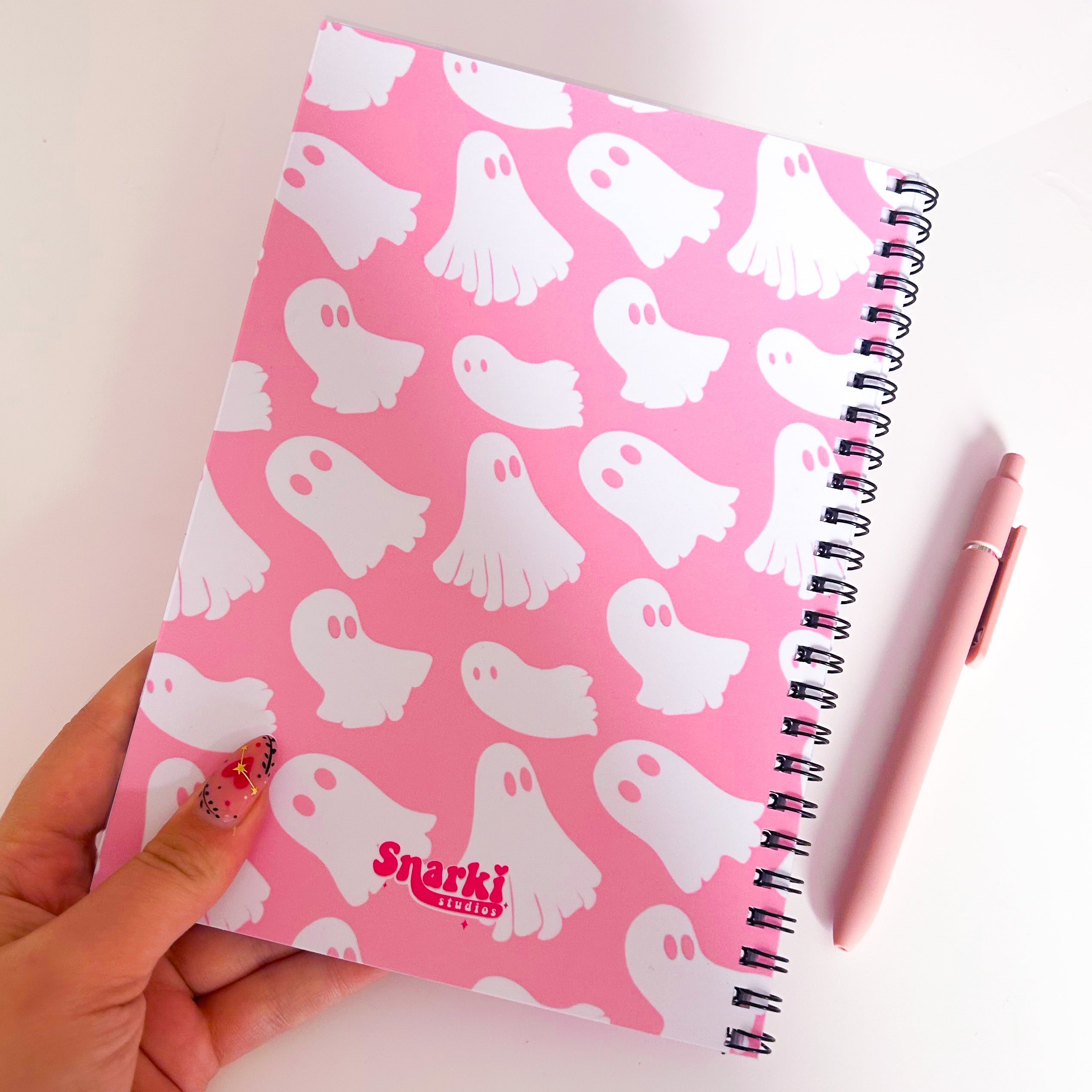 Pink notebook with ghost pattern held by a hand, Snarki brand visible
