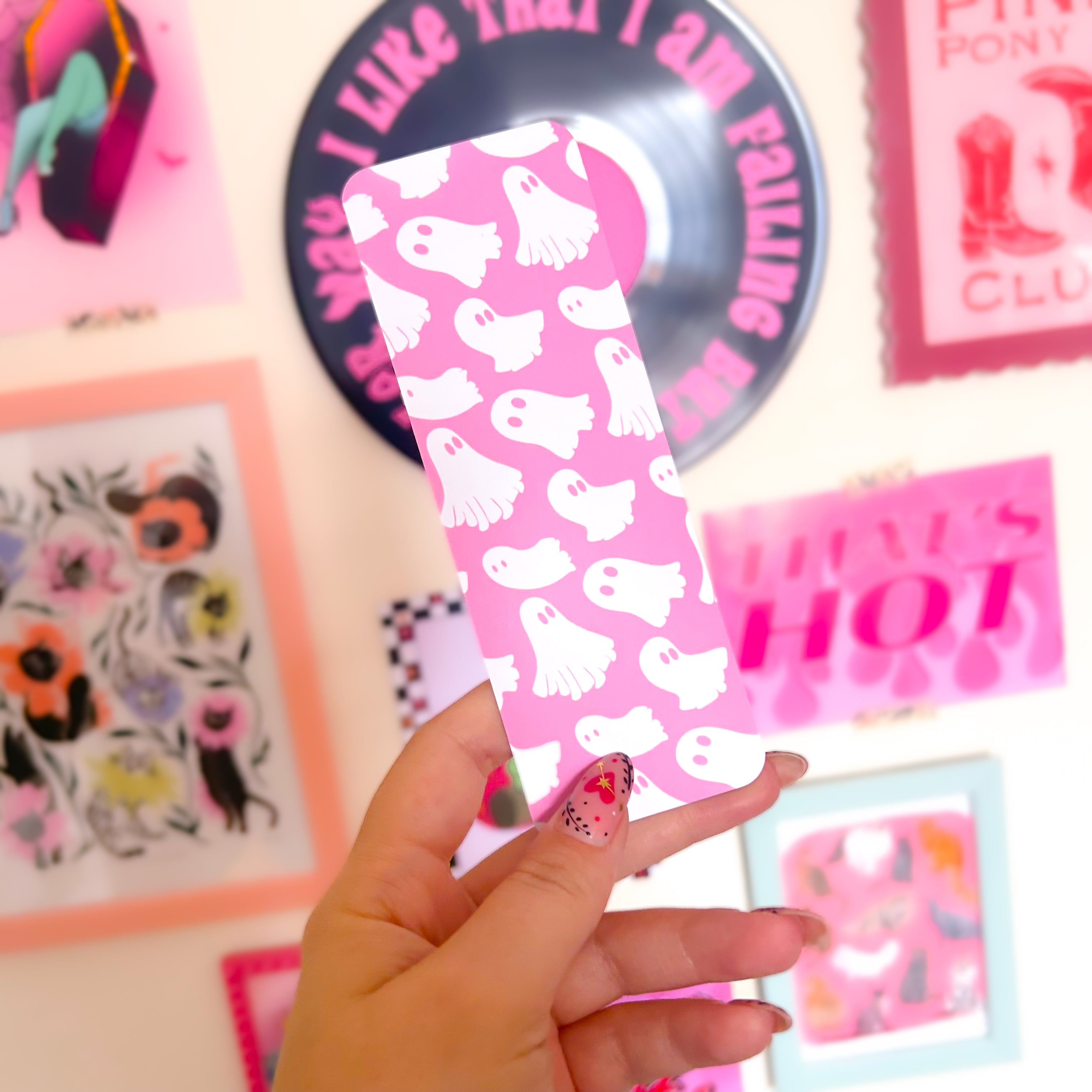 Pink bookmark with white ghost pattern held by a hand against a colorful background.