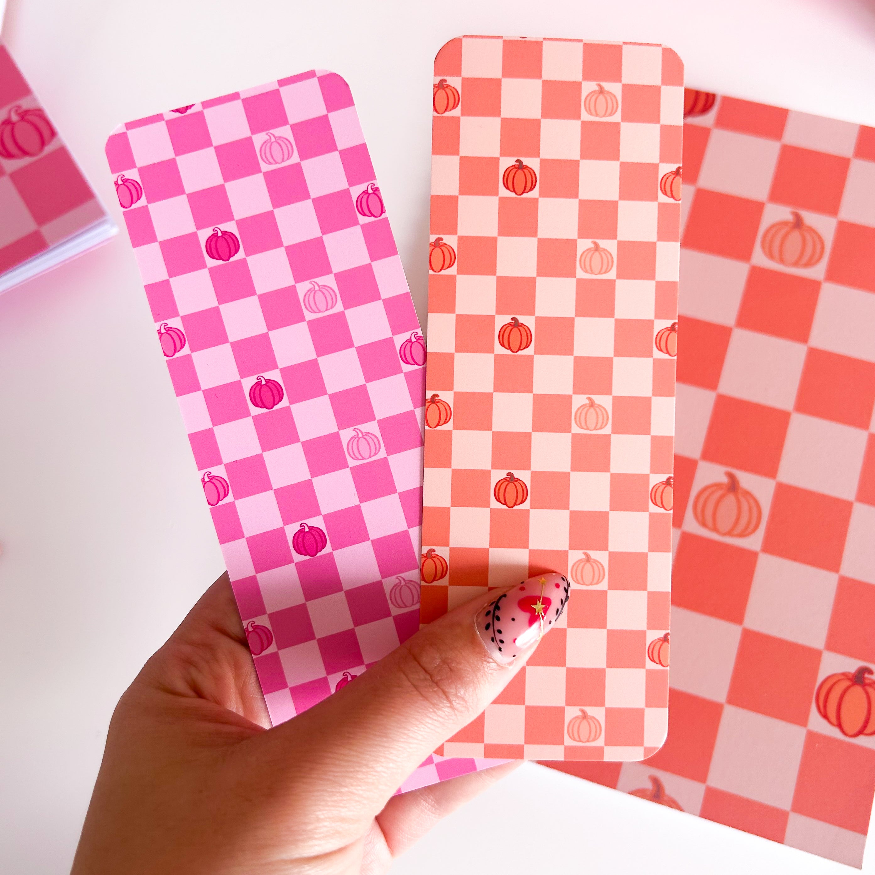Checkered Bookmarks in pink and orange with pumpkin designs held by a hand on a light background