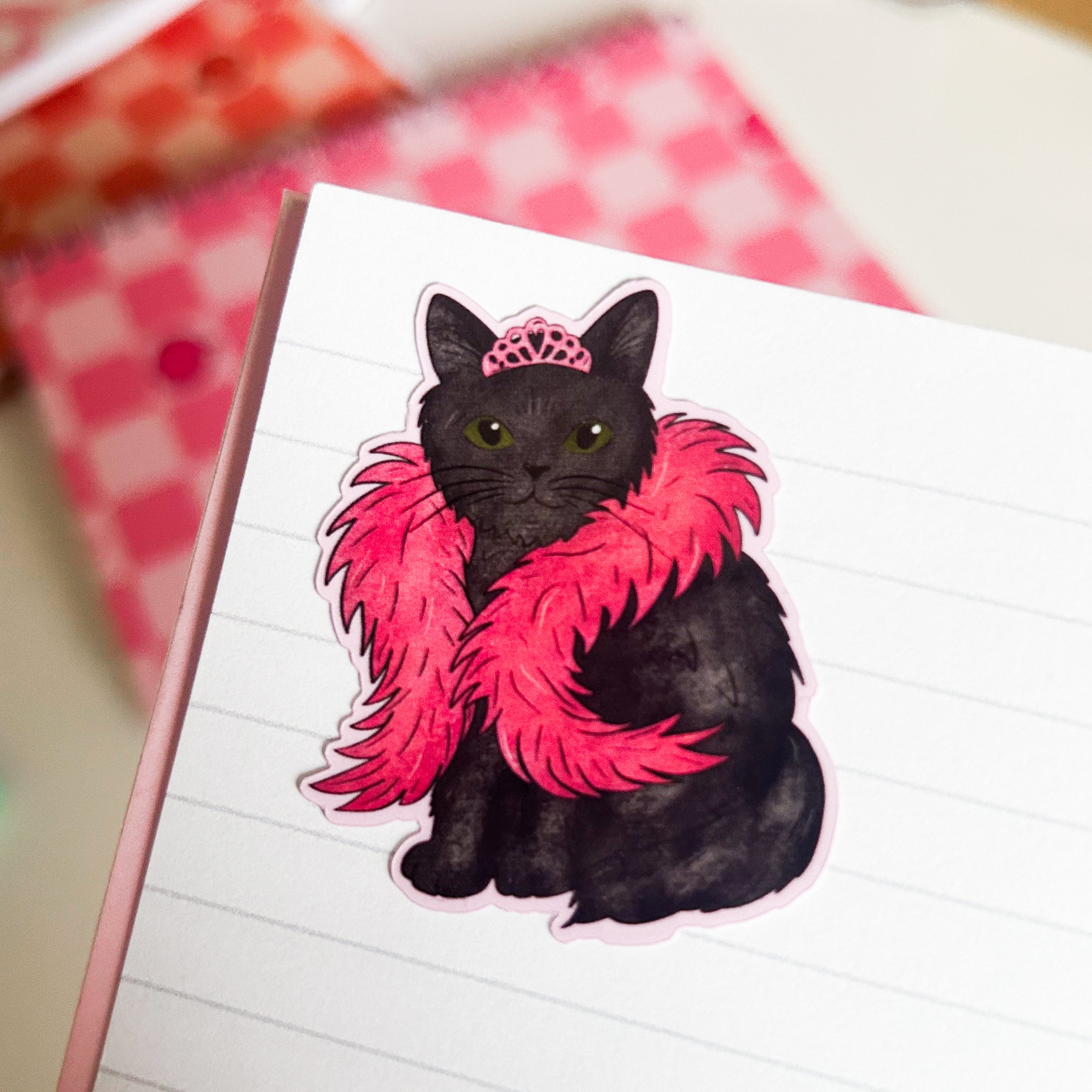 Black cat sticker with pink boa and tiara on a notebook